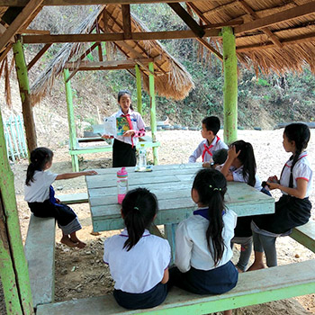A girl reads aloud outdoors to other children at Big Sister Mouse school in Laos