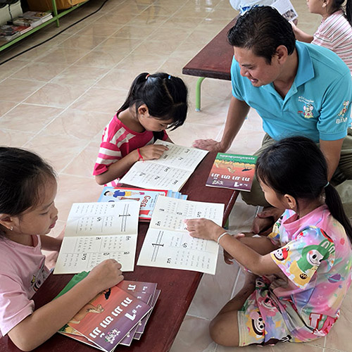 A teacher and three children at a low table, children looking at books