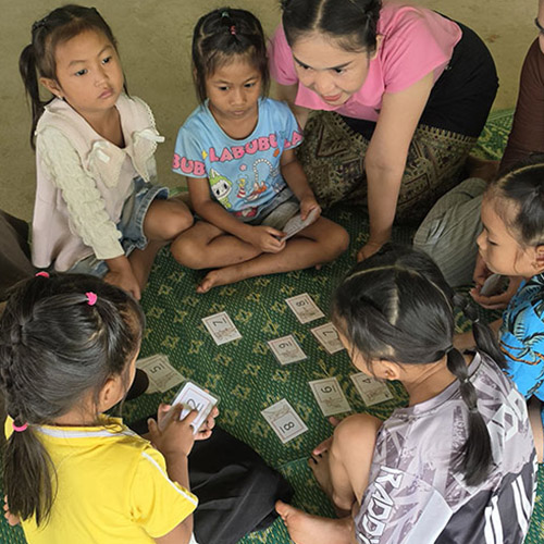 Cards with numbers are face-up on the table, children sitting around them.