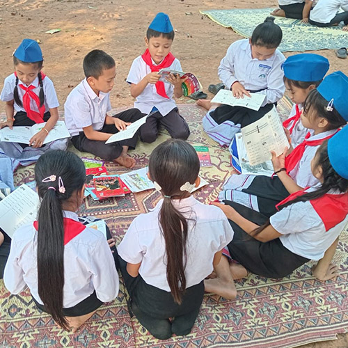 Children sitting in a circle outside looking at books together
