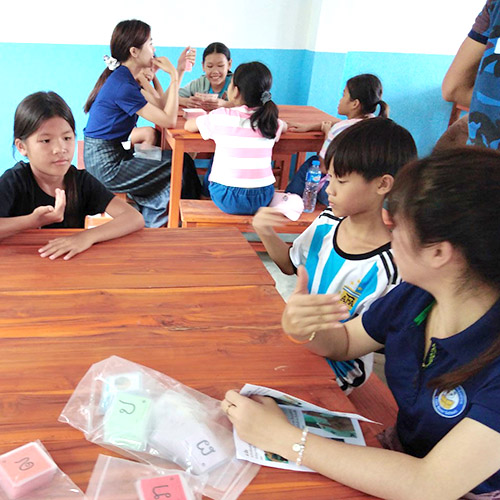 A teacher and several small children holding up hand signs
