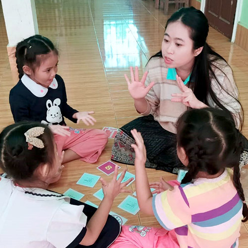 A teacher and several small children learn numbers, with cards in front of them