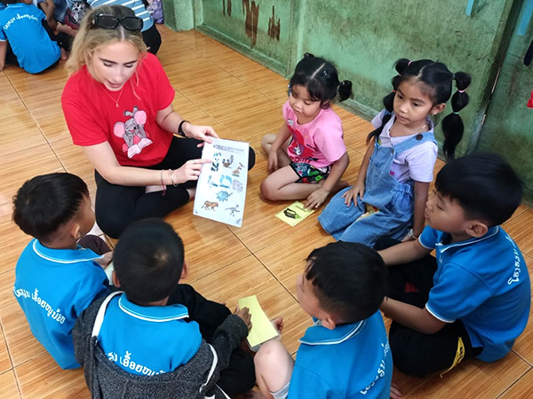 A woman holds up a large card with animal pictures, showing a group of Lao children the names